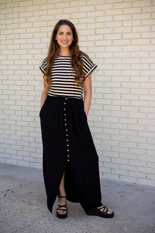 Woman wearing a striped shirt and black skirt standing against a white brick wall.